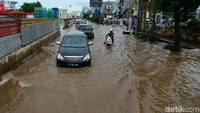 Pengendara mendorong motornya di antara mobil yang nekat menerobos banjir.