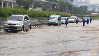 Pengendara memperlambat laju kendaraan saat melintasi banjir di jalan tersebut.