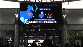 Para penumpang berjalan di bawah monitor yang menampilkan informasi tentang virus corona stasiun kereta cepat di Seoul, Korea Selatan. Foto: Getty Images