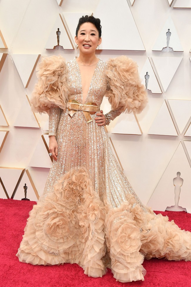 Aktris Sandra Oh memilih gaun rancangan Elie Saab untuk red carpet Oscar 2020. Gaun berwarna champagne itu dihiasi sequin dan payet berkilauan, ditambah aksen pita dan ruffle pada bagian lengan dan rok. Terlalu banyak detail membuat penampilan Sandra Oh terkesan berat dan penuh. Foto: Amy Sussman/Getty Images