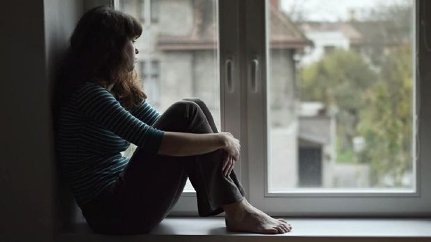 Sad young woman sitting on the window