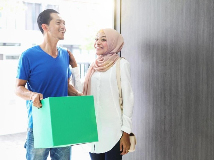 ilustrasi pasangan suami - istri Couple moving in to new house, carrying a box and looking surprise when opening a door.