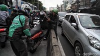Dua orang pemotor bahu membahu mengangkat sebuah motor keluar dari jalur Bus TransJakarta demi terhindar dari razia polisi, Rabu (12/2/2020).