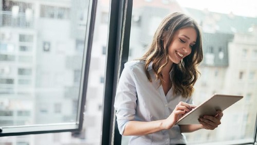 Young businesswoman using a digital tablet while standing in front of windows in office