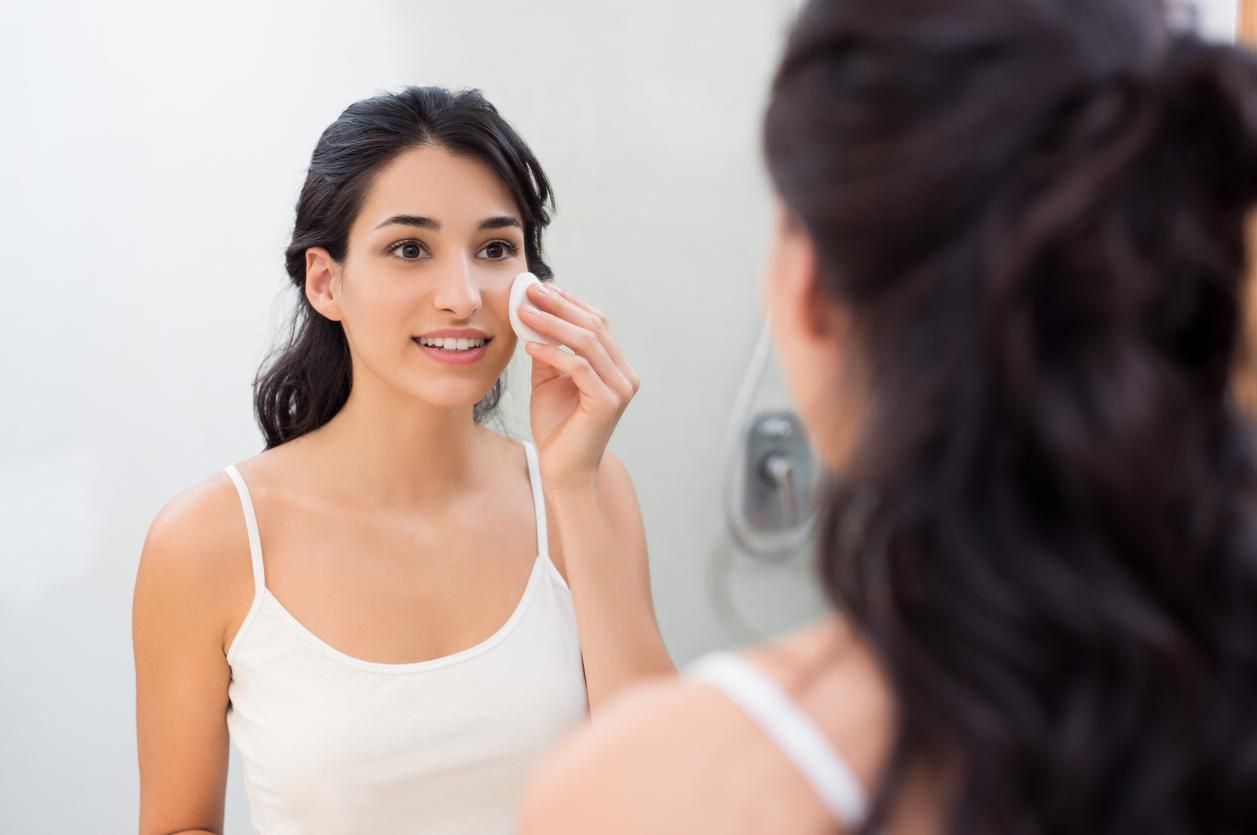Healthy fresh girl removing make up from her face with cotton pad. Smiling girl cleaning her face in bathroom. Beautiful healthy woman making scrub on her face.