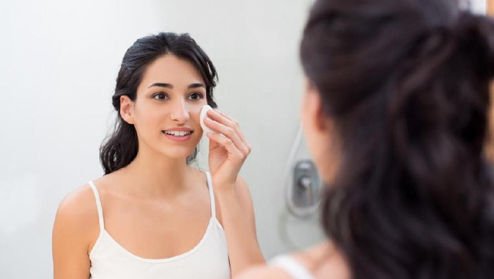 Healthy fresh girl removing make up from her face with cotton pad. Smiling girl cleaning her face in bathroom. Beautiful healthy woman making scrub on her face.