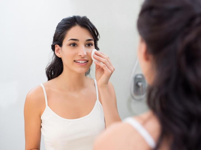 Healthy fresh girl removing make up from her face with cotton pad. Smiling girl cleaning her face in bathroom. Beautiful healthy woman making scrub on her face.