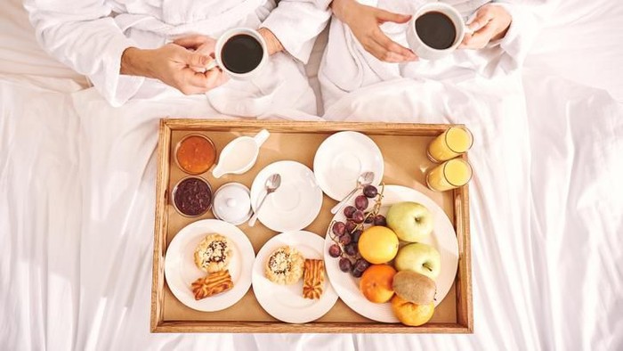 sarapan romantis Closeup front view of a mid 20s happy couple watching tv in bed on lazy weekend morning. They are eating some snacks and having sodas. The guy is changing the channels.