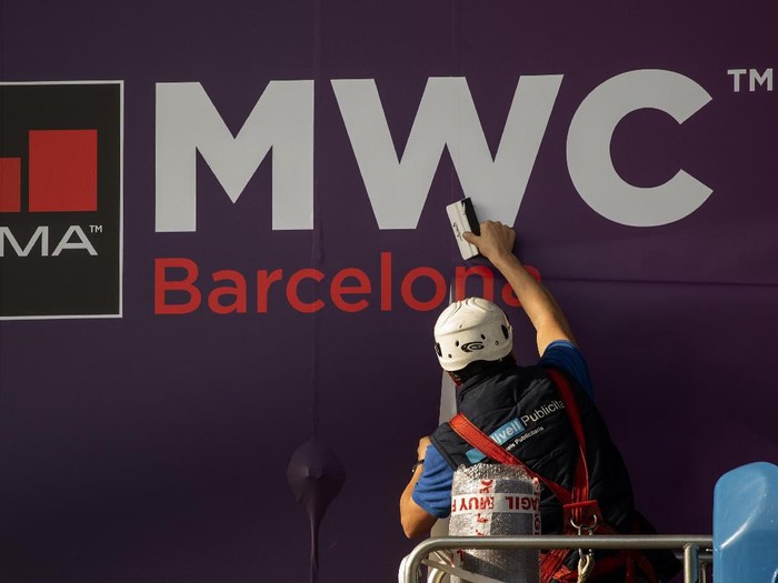 MWC A worker fixes a poster announcing the Mobile World Congress 2020 in a conference venue in Barcelona, Spain, Tuesday, Feb. 11, 2020. Intel Mobile is the latest company announcing that is pulling out of the Mobile World Congress scheduled to be held in Barcelona in late February. Authorities still seem to be committed to hold it, meeting foreign diplomats on Tuesday to brief on the efforts to prevent any spread of the new coronavirus virus during the industry show. (AP Photo/Emilio Morenatti)