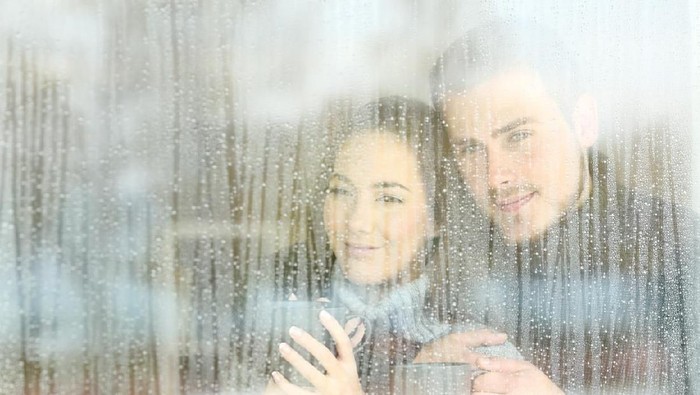 Satisfied couple looking through a window at home in a rainy day