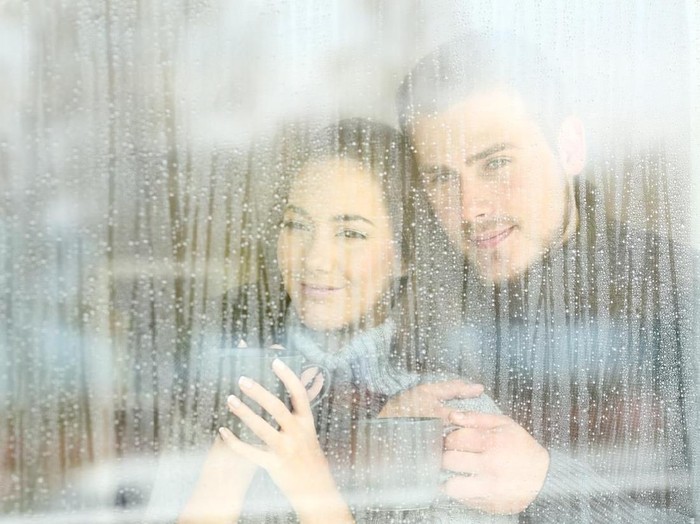 Satisfied couple looking through a window at home in a rainy day