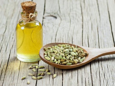 Glass bottle of fennel essential oil with fennel seeds in wooden spoon on wooden table. Herbs alternative medicine background concept