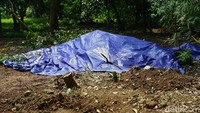 Di lokasi itu terdapat sebuah gundukan tanah yang ditutupi oleh terpal warna biru. 
