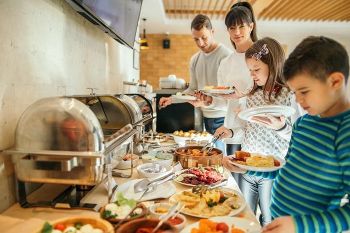Family taking food in self service restaurant in hotel. A lot of domestic colorful food is served. Family with two children.