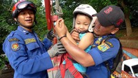 Dua orang petugas damkar membantu seorang anak yang hendak menjajal flying fox.