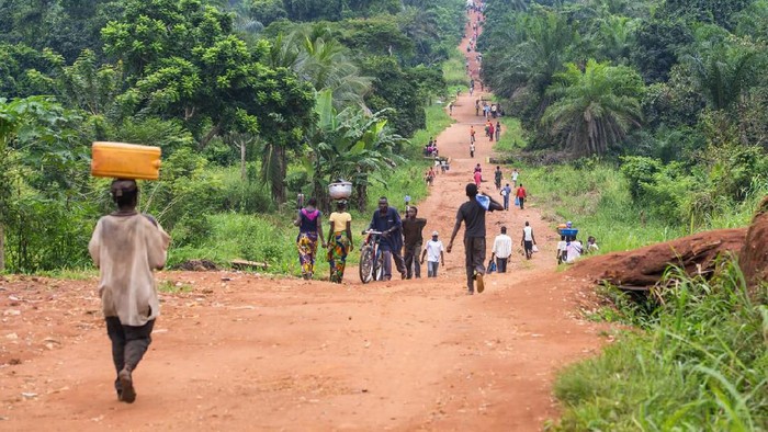 Karawa, Democratic Republic of Congo - August 24, 2013: An upaved road in rural Congo, a lot of people are walking on the road which connects two villages in the province of Equateur. Walking and bicycling is nearly the only way of transportation in the poor regions of Congo. Mostly women are carrying heavy loads of goods on their heads when they are walking to a market place.