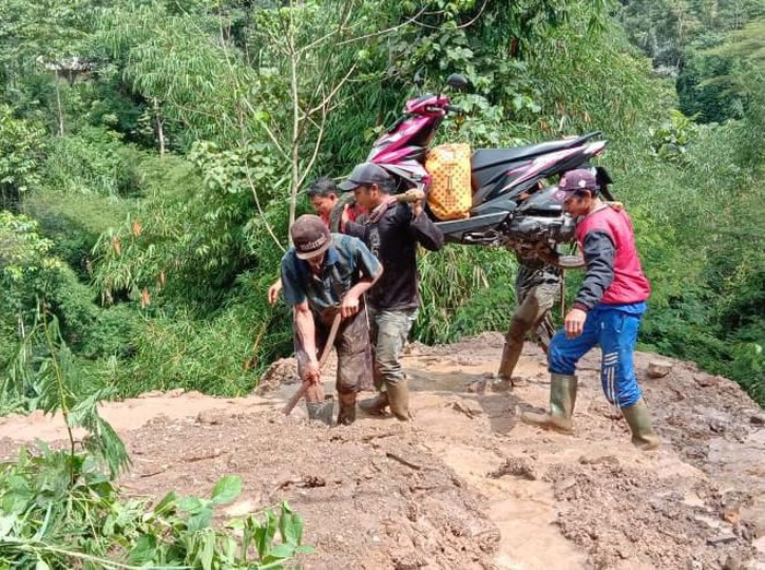Sejumlah warga mengangkut motor melintasi material longsor di Garut