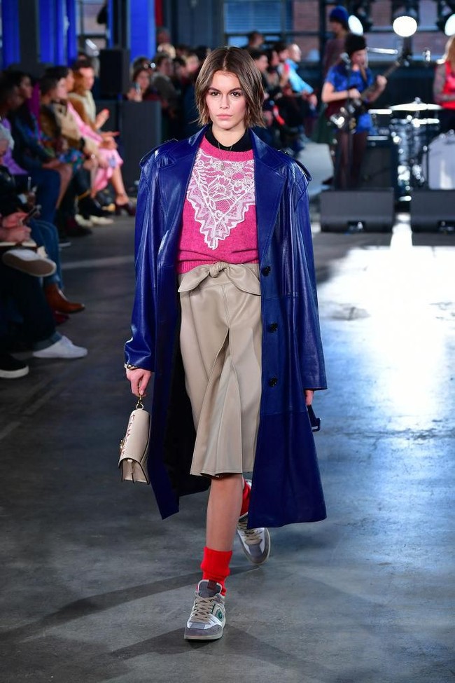 Tampil lebih kasual, Kaia Gerber mengenakan coat patent leather dipadu blouse rajut dan rok kulit. Perpaduan gaya sporty dan chic menghasilkan nuansa eklektik pada koleksi busana Coach. Foto: Slaven Vlasic/Getty Images