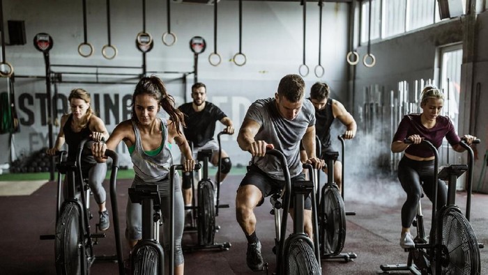 Ilustrasi crossfit Large group of athletic people having sports training on exercise bikes in a gym