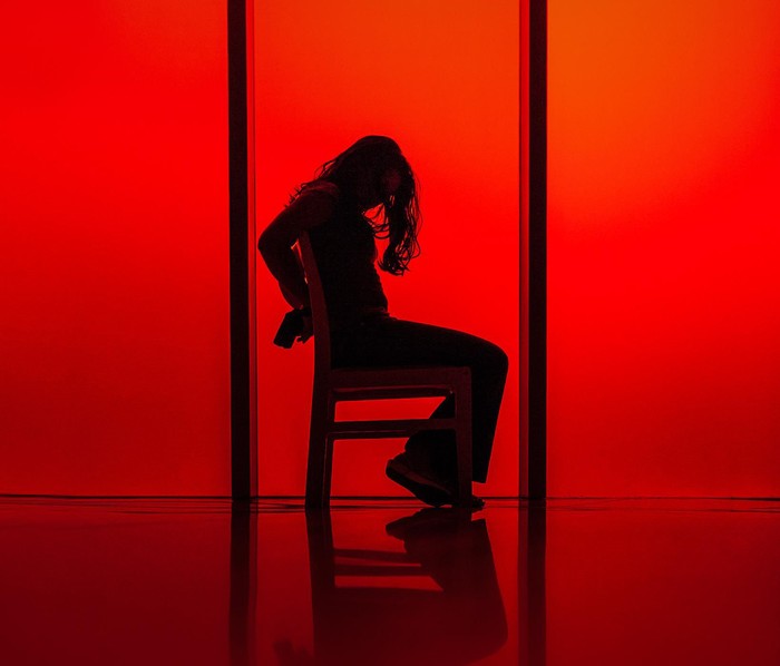 silhouette of a woman tied up to a chair against a red background