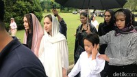 Bunga menggandeng putranya, Noah Sinclair yang juga mengenakan busana serba putih saat dipayungi oleh saudarinya, Intan Ayu.