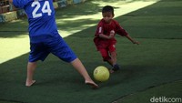 Seorang anak berkaos Persija Jakarta tengah berusaha melewat hadangan bek lawan.