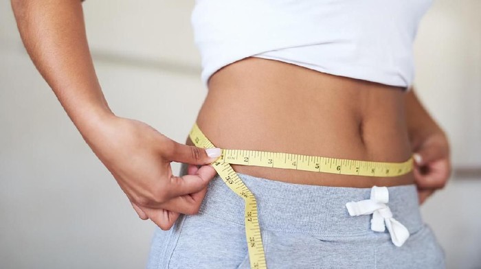 Diet Cropped shot of a young woman measuring her waist in the bathroom