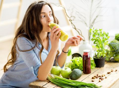 Beautiful woman sitting with healthy green food and drinking smoothie at home. Vegan meal and detox concept