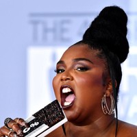 Lizzo lalu menyempurnakan gayanya dengan clutch berbentuk batangan coklat dengan tulisan 100%. Besar kemungkinan angka tersebut diambil dari lirik lagunya yang berjudul Truth Hurts: Im 100 percent that b----. (Foto: Gareth Cattermole/Getty Images)