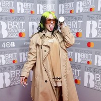 Billie Eilish membungkus tubuhnya dengan tracksuit coklat yang dihiasi dengan detail cincin yang berjajar di area neckline dan keliman atasannya. Busana rancangan Riccardo Tisci itu lalu dilengkapi luaran berupa trench coat klasik Burberry dalam versi modern dengan detail cincin yang sama. (Foto: Ian West/ PA via AP)