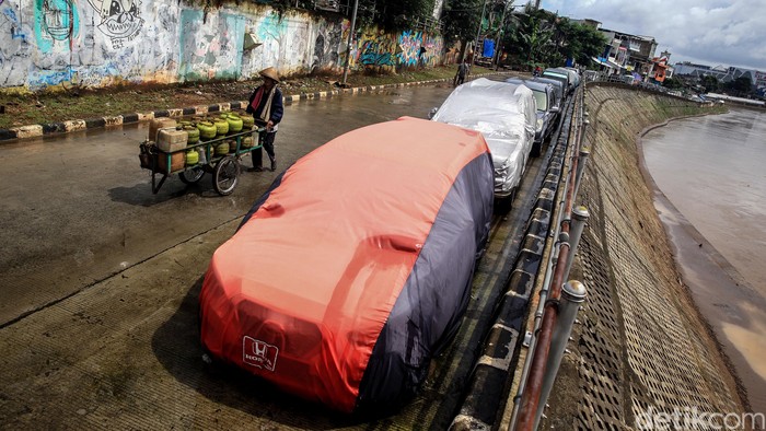 Jalan Bekas Normalisasi Kali CIliwung Jadi 'Garasi Mobil' Warga memarkir kendaraan roda 4 di jalan Inspeksi Kali Ciliwung, Jakarta, Jumat (21/2/2020). Jalan tersebut merupakan hasil normalisasi pelebaran sungai Ciliwung di kawasan Kampung Pulo (sisi timur) dan Bukit Duri (sisi barat) beberapa waktu lalu. Namun, arus lalu-lintas yang tidak ramai membuat warga menjadikan satu lajur jalan sebagai lahan parkir tetap layaknya garasi mobil di rumah. Beberapa menggunakan penutup badan mobil untuk menghindari sinar matahari dan hujan. Rumah di sisi jalan hanya gang yang tidak terdapat akses untuk mobil.