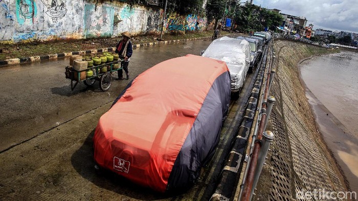 Warga memarkir kendaraan roda 4 di jalan Inspeksi Kali Ciliwung, Jakarta, Jumat (21/2/2020). Jalan tersebut merupakan hasil normalisasi pelebaran sungai Ciliwung di kawasan Kampung Pulo (sisi timur) dan Bukit Duri (sisi barat) beberapa waktu lalu. Namun, arus lalu-lintas yang tidak ramai membuat warga menjadikan satu lajur jalan sebagai lahan parkir tetap layaknya garasi mobil di rumah. Beberapa menggunakan penutup badan mobil untuk menghindari sinar matahari dan hujan. Rumah di sisi jalan hanya gang yang tidak terdapat akses untuk mobil.