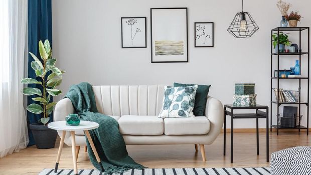 Black table next to sofa with green blanket in cozy apartment interior with gallery of posters