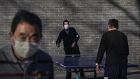 Sejumlah warga mengenakan masker saat bermain tenis meja di kawasan Beijing, China. Getty Images/Kevin Frayer.
