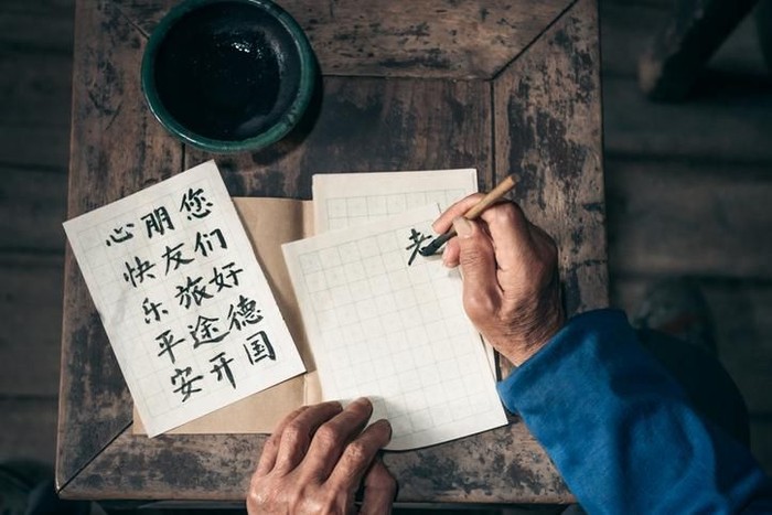 close up of old hands writing chinese calligraphy characters with india ink on paper