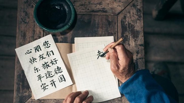 close up of old hands writing chinese calligraphy characters with india ink on paper