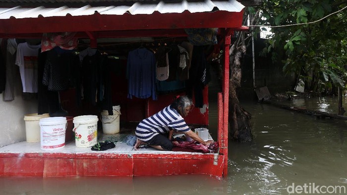 Warga melintasi banjir di RT 10 RW 05 Kelurahan Rawa Terate, Cakung, Jakarta Timur, Senin (24/2/2020). Banjir dikawasan ini sudah melanda sejak minggu 23 Februari hingga kini belum surut. Kemarin ketinggian air mencapai 2,5 m dan hari ini masih mencapai 60 cm. Menurut salah satu warga Sri Aminah hingga hari ini mereka belum mendapat bantuan dan mereka membutuhkan air bersih dan makanan. listrik dikawasan ini pun padam.