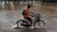 Seorang warga menggowes sepedanya melintasi jalan yang terendam banjir sejak Minggu (23/2/2020).