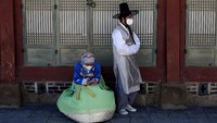 Dua orang wisatawan mengenakan pakaian tradisional dan menggunakan masker pelindung pernapasan saat berkunjung ke Gyeongbok Palace di Seoul, Korea Selatan. Getty Images/Chung Sung-Jun.