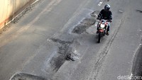 Air hujan dan beban kendaraan membuat aspal mengelupas.