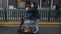 Sepasang pria dan wanita di China tampak mengenakan masker saat sedang mengendari skuter di jalanan Beijing, China. Getty Images/Kevin Frayer.