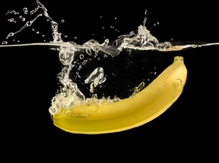Ripe yellow banana splashing into clear water, black background