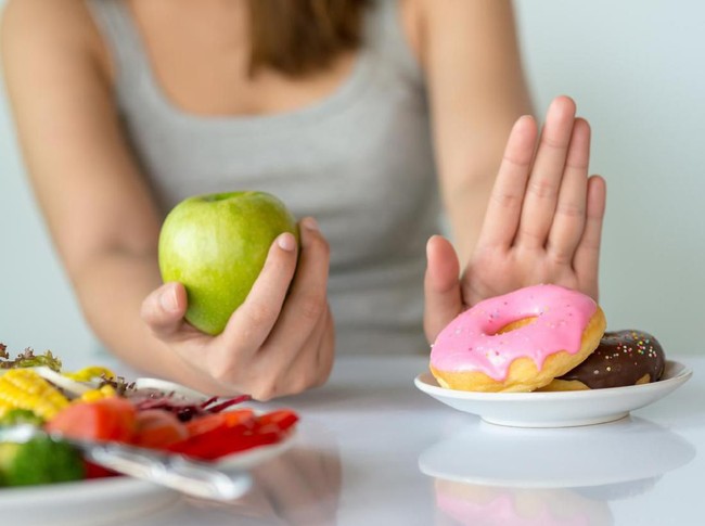 Dieting or good health concept. Young woman rejecting Junk food or unhealthy food such as donut or dessert and choosing healthy food such as fresh fruit or vegetable.