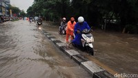 Seorang petugas membantu pengendara yang motornya mogok usai nekat menerobos banjir di Jalan Perjuangan, Kebon Jeruk, Jakarta Barat.