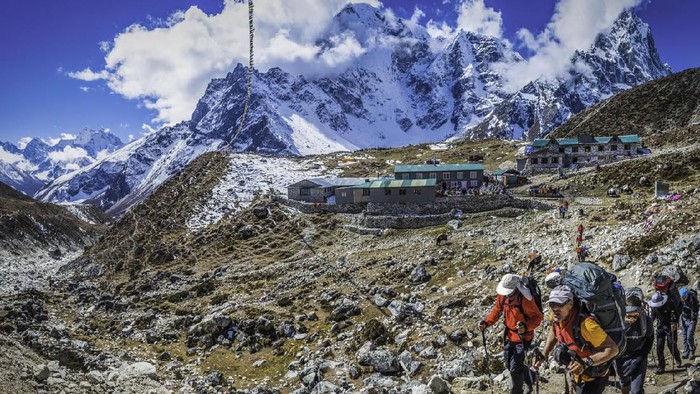 Lobuche, Nepal - 27th October 2014: Team of mountaineers trekking through the rocky moraine of the Khumbu valley along the Everest Base Camp trail from traditional teahouses overlooked by the vertiginous north faces of Taboche (6495m) and Cholatse (6440m) deep in the Himalaya mountain wilderness of the Sagarmatha National Park, a UNESCO World Heritage Site, Nepal. Composite panoramic image created from five contemporaneous sequential photographs.