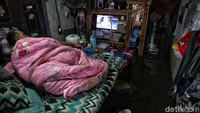 Seorang warga tengah menonton televisi sambil berbaring dan berselimut meski air menggenangi bagian dalam rumahnya yang berada di kawasan Semper Barat, Jakarta Utara, Selasa (25/2/2020).