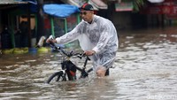 Seorang warga menuntun sepedanya melintasi banjir setinggi lutut.