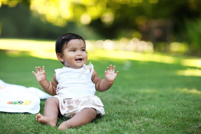 nama bayi Happy smiling baby girl lying on blanket in green grass of tulips field. Child playing outdoors in spring park. Image of Mothers Day, Easter. Family on nature in Arboretum, Slovenia, Europe.
