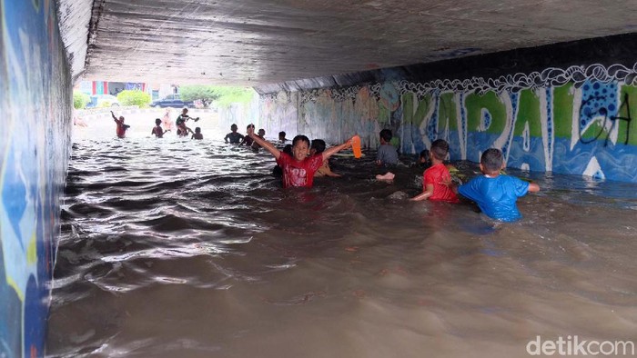 Banjir akibat hujan deras membuat Underpass Gonggo, Karawang, berubah seperti kolam renang. Anak-anak pun tampak asyik berenang di sana.