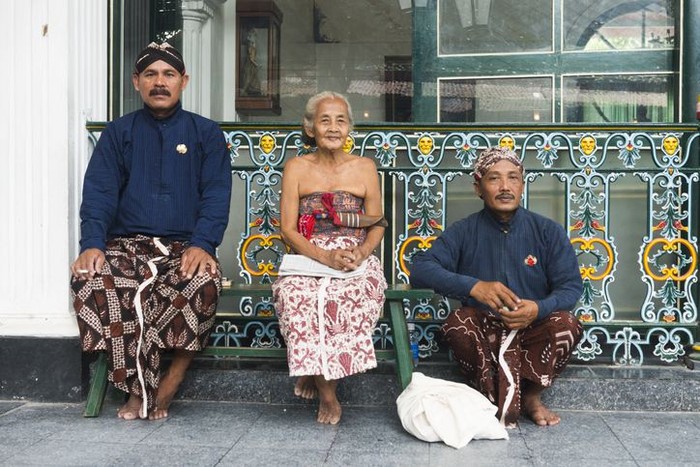 Yogyakarta, Indonesia - April 6, 2015: Three Javanese people wearing traditional clothing sit outside during a break while working at the Sultans Palace in Java, which is also called the Kraton. The two men wear head cloths and sarongs. The senior woman who sits in the middle wears a light colored sarong.
